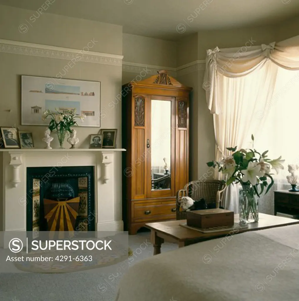 Edwardian wardrobe with mirrored door in bedroom with white swagged curtains and white fireplace