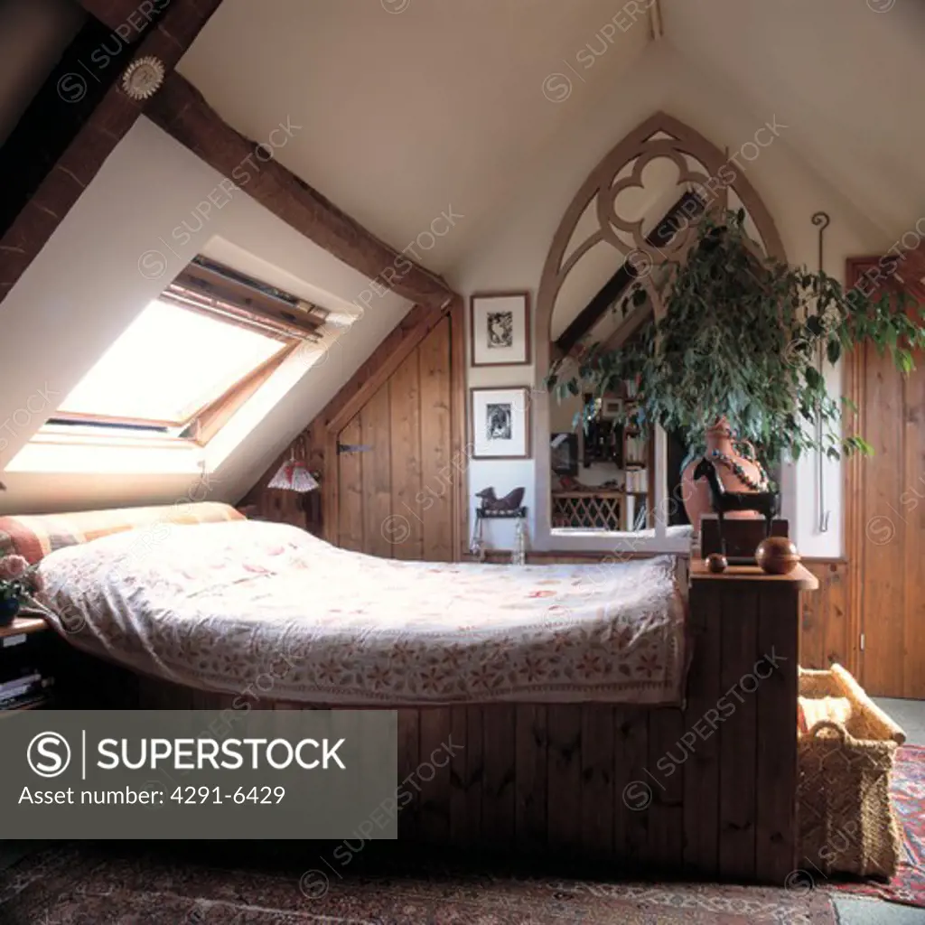Bed below Velux window in attic bedroom with houseplant in front of Gothic mirror
