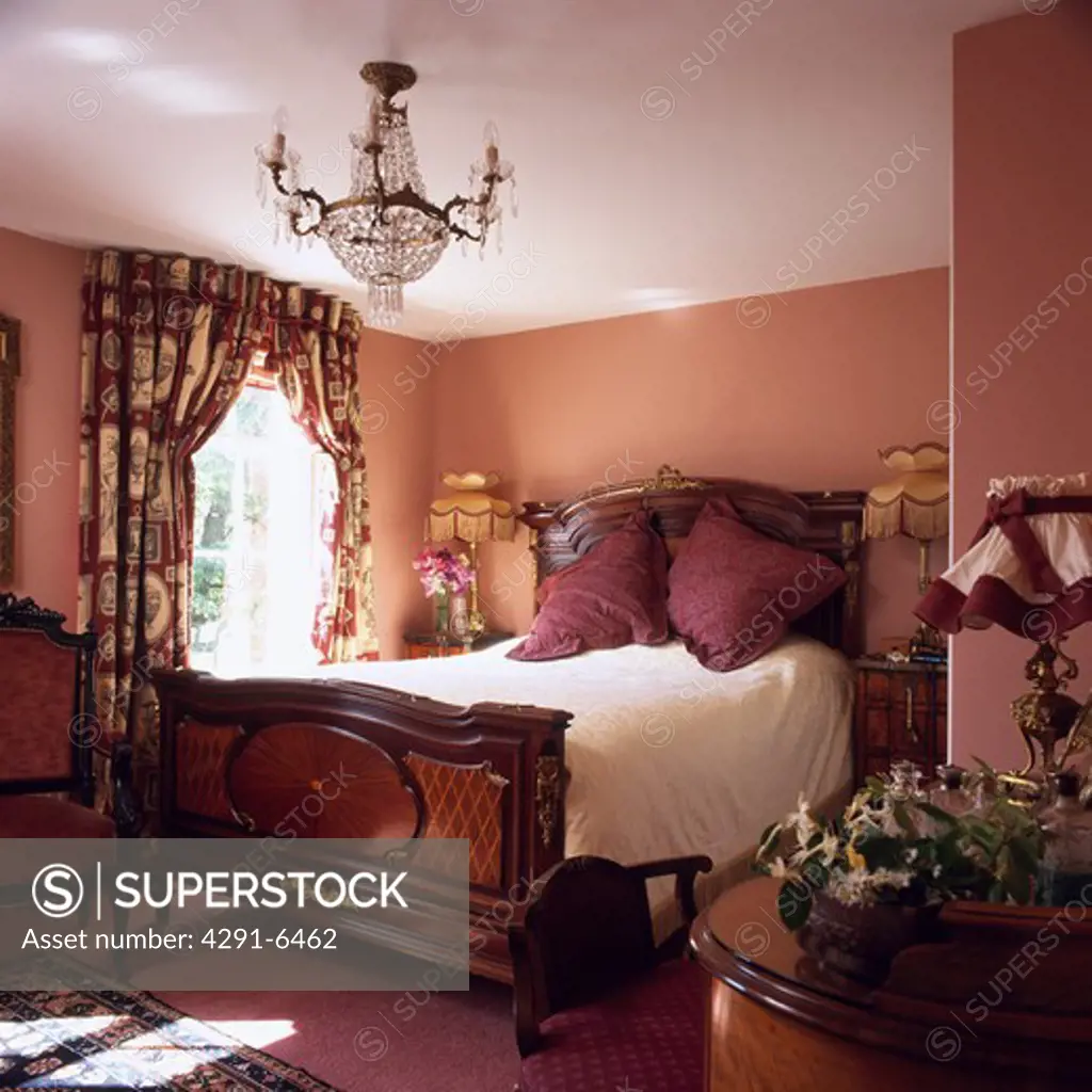 Antique mahogany bed and floral curtains in small dark pink bedroom with antique glass chandelier