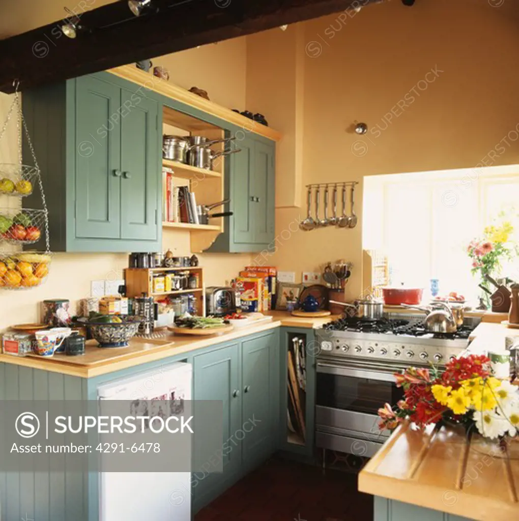 Stainless steel range oven and small refrigerator in cottage kitchen with green painted wooden fitted cupboards