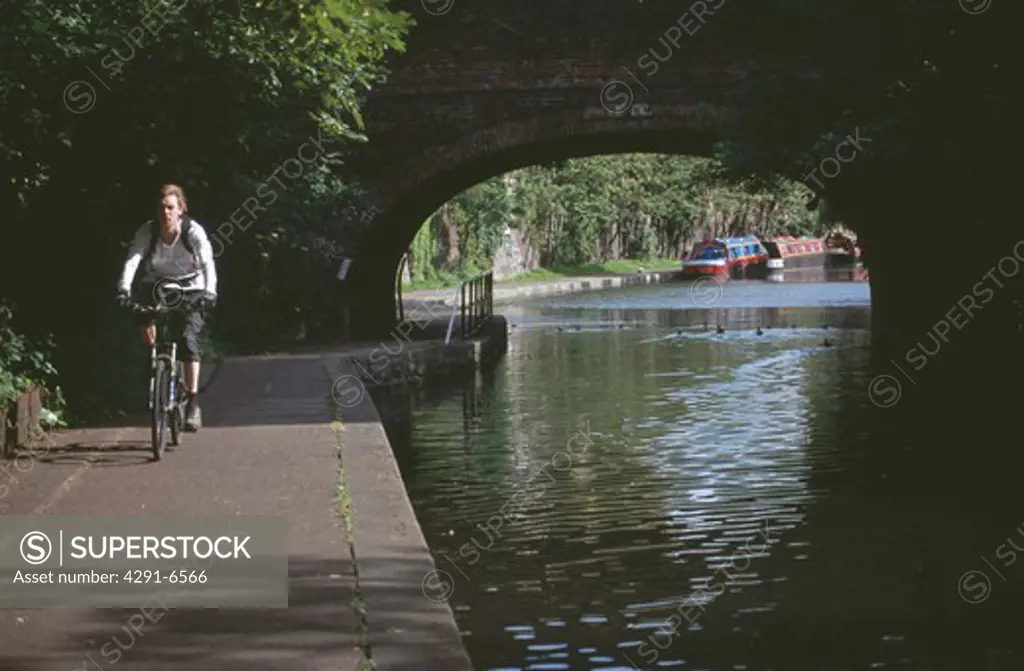 Young woman cycling on towpath beside the Regent Canal in London