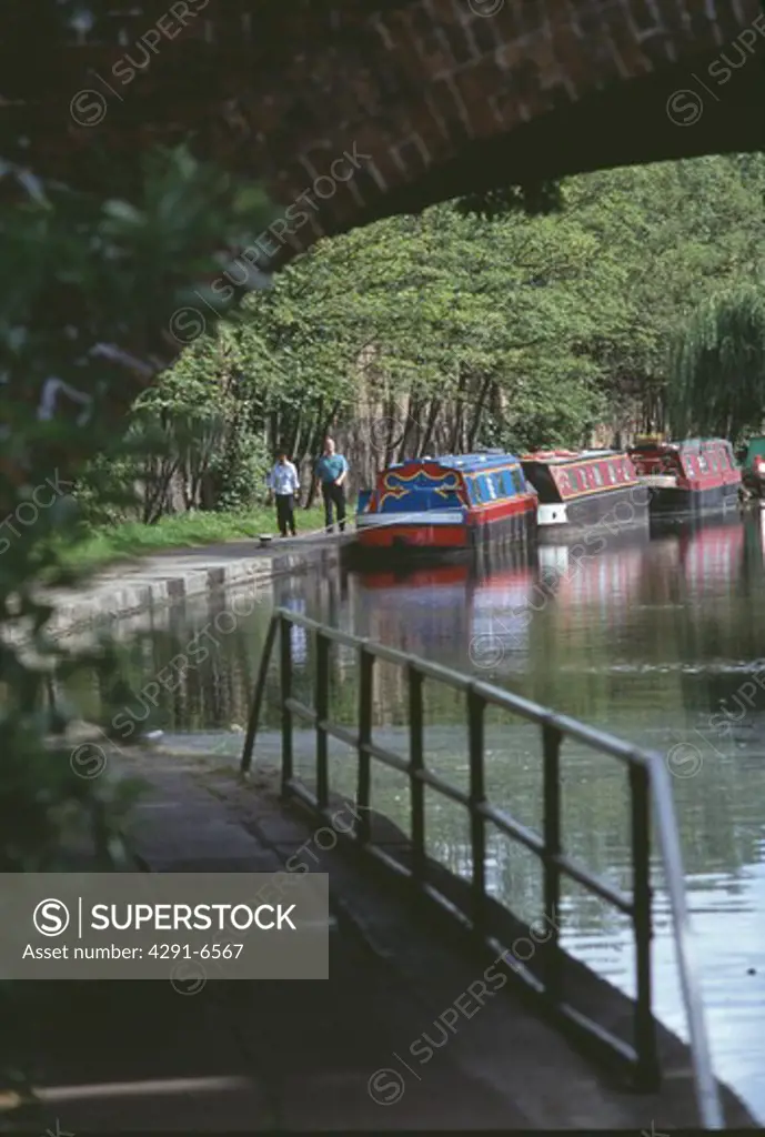 Footpath below bridge over the Regent Canal in London with narrow boats moored on the bank