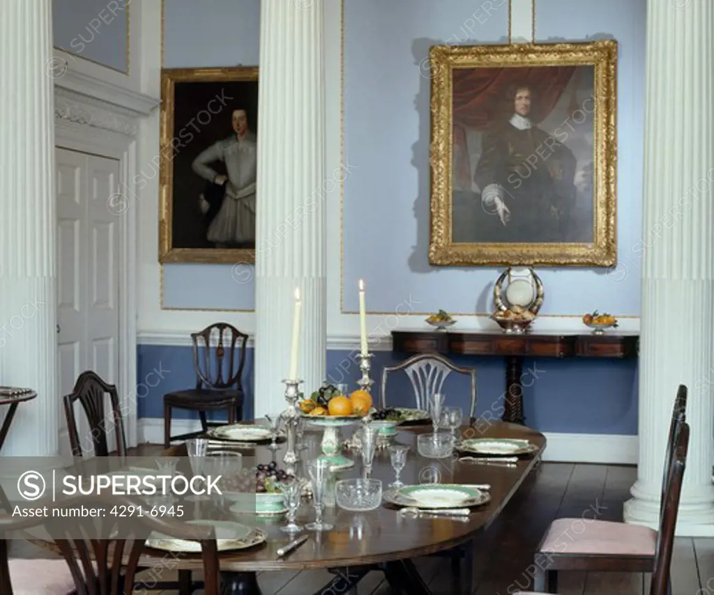 Table settings on mahogany table in pastel blue diningroom with pillars and portrait paintings on the wall