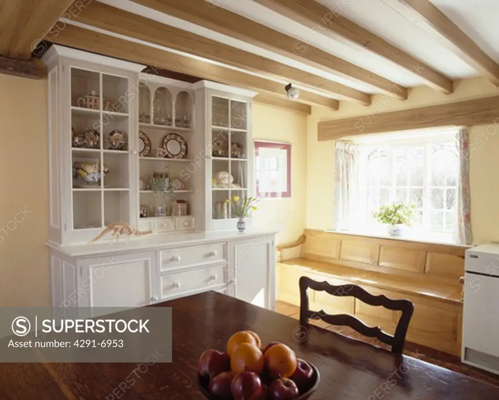 Fitted white dresser and pine windowseat in country kitchen dining room with beamed ceiling