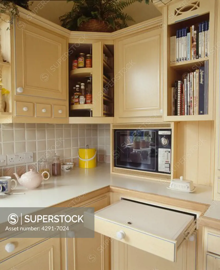 Close-up of pull-out shelf in small kitchen with pale wood units and microwave oven
