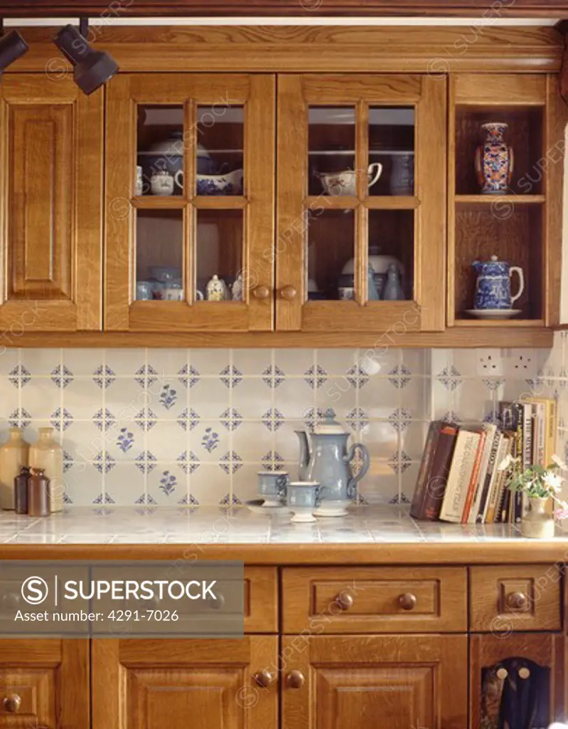 Close-up of white and blue wall-tiles and pale wood fitted units in small kitchen