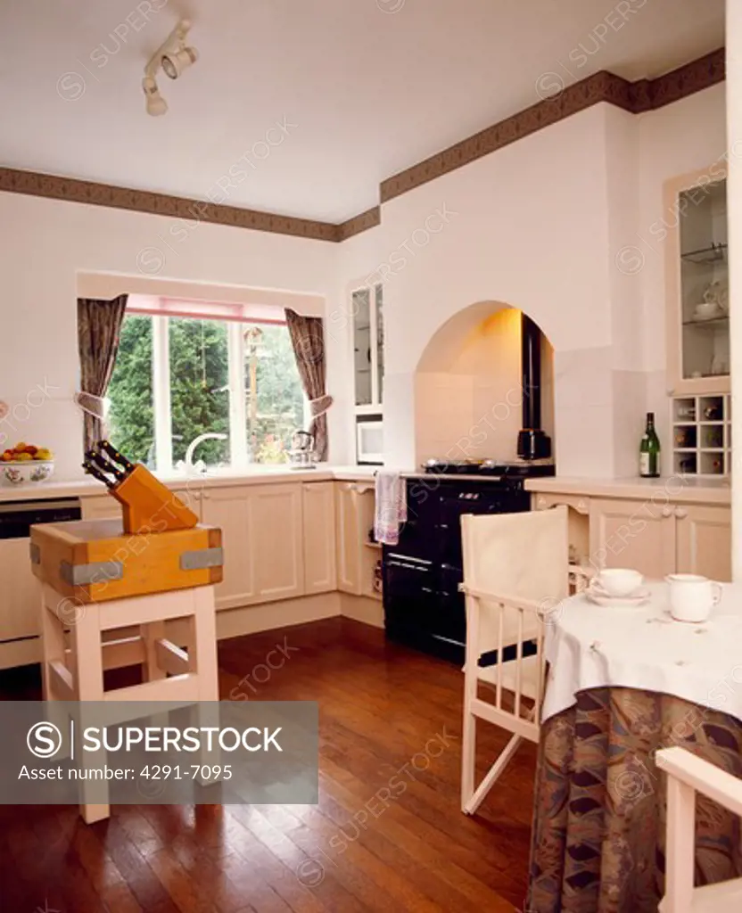 Butcher's block and wooden flooring in country kitchen with director's chairs at table with white cloth