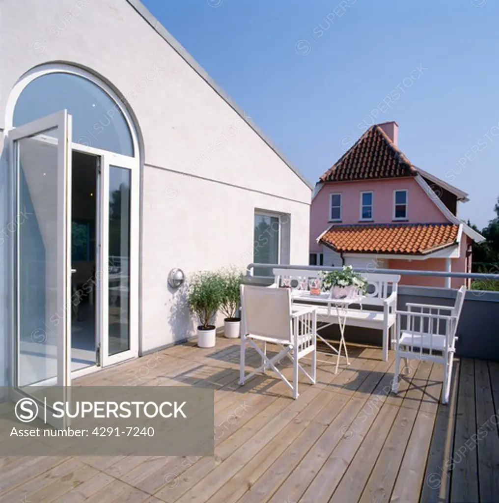 Director's chairs and white bench on large decked balcony of house with glass patio doors