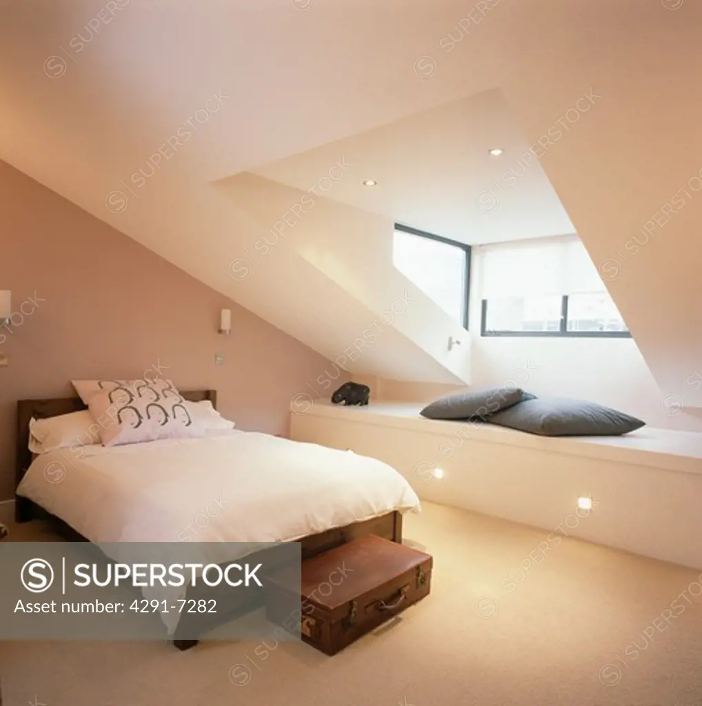 Cream duvet on bed in modern attic bedroom with cream carpet fitted storage below dormer window
