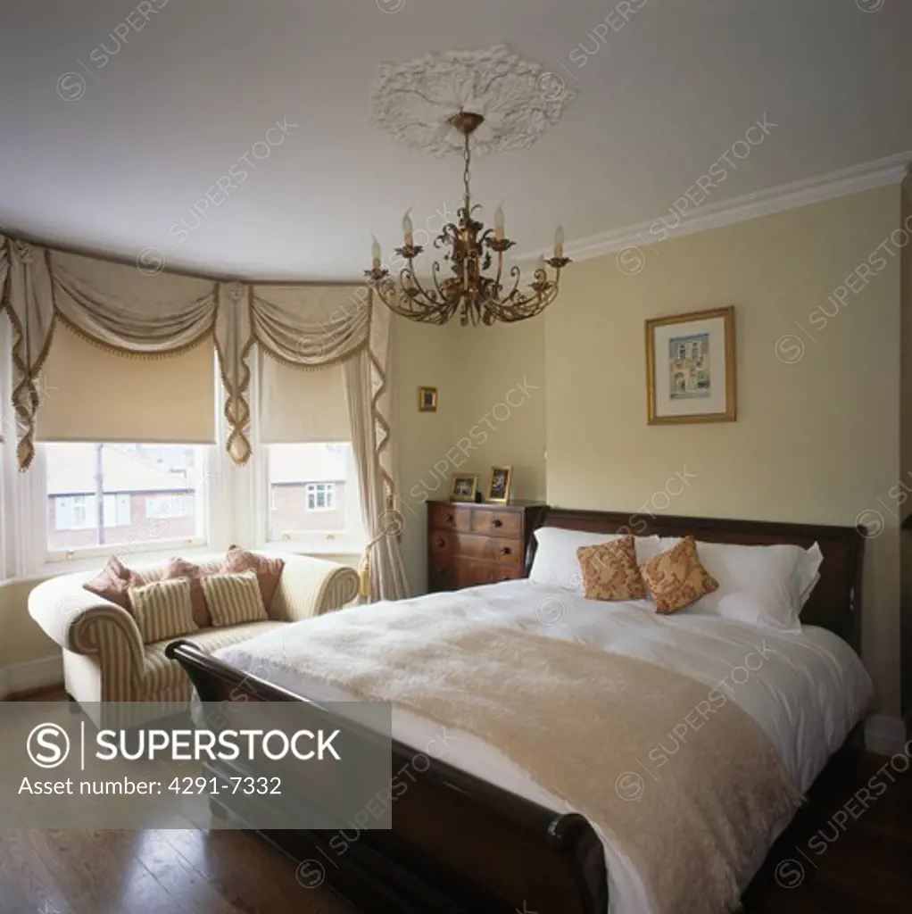 Chandelier above lit bateau bed with cream bedlinen in townhouse bedroom with cream blind on bay window