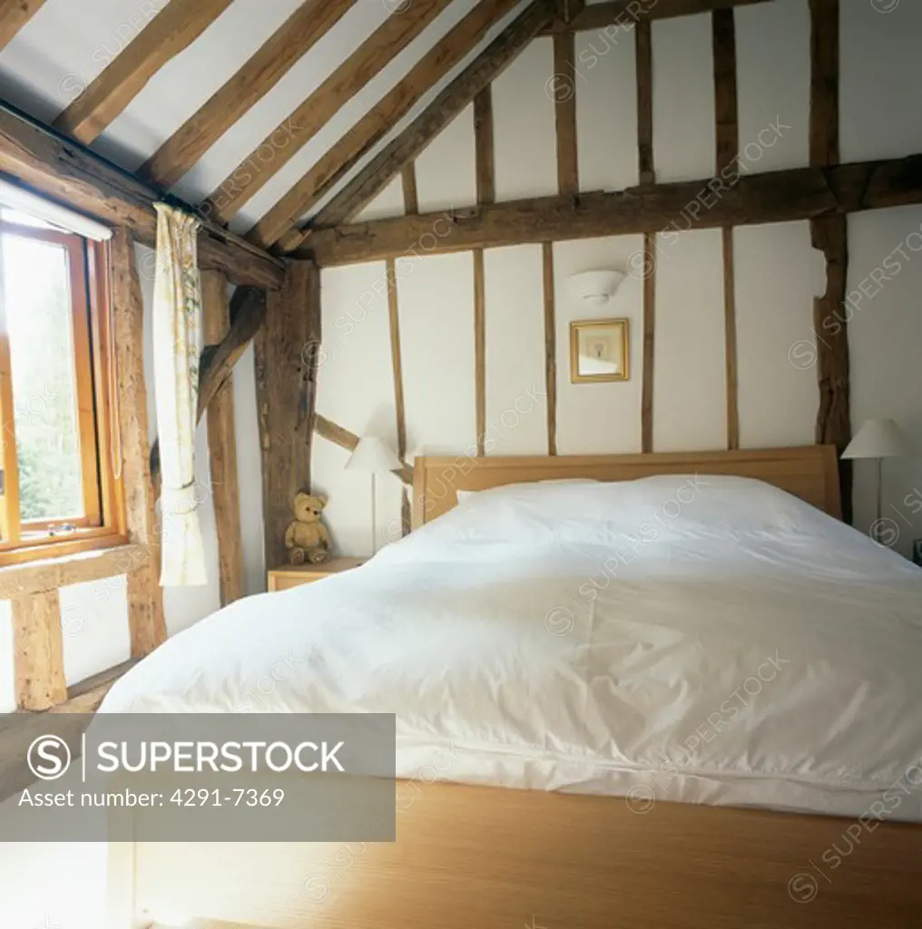 White duvet on simple wooden bed in beamed country bedroom with apex ceiling