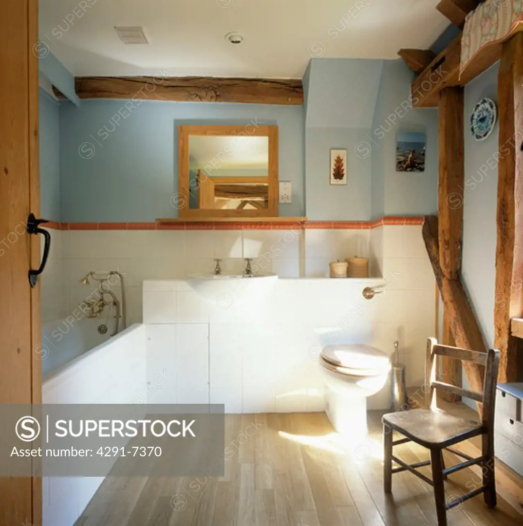 Small wooden chair in pastel blue and white country bathroom with wooden flooring