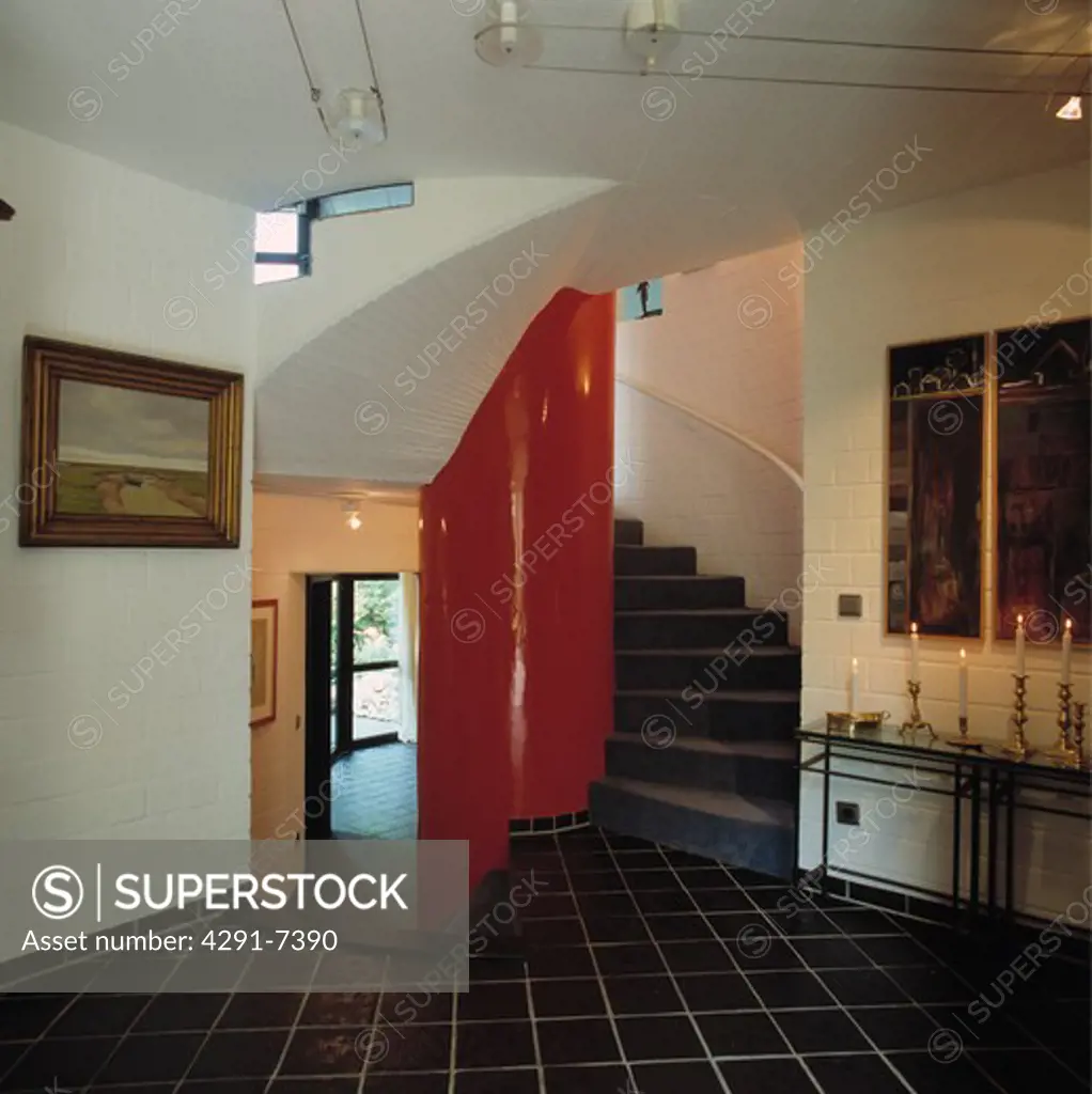 Black ceramic floor tiles in hall with red painted curved wall on staircase