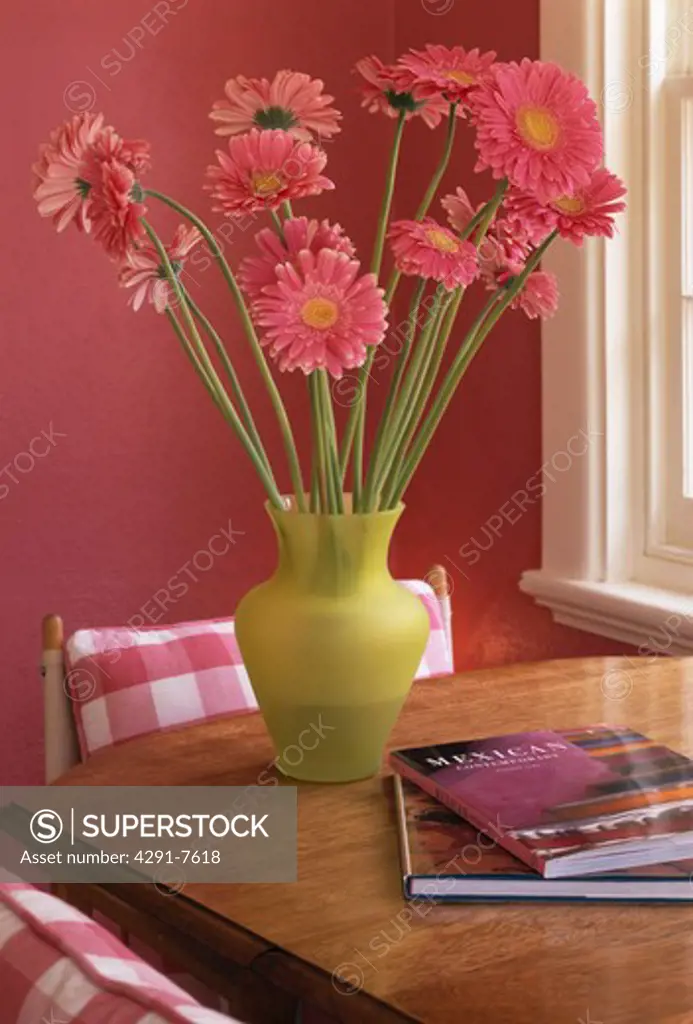 Close-up of pink gerberas in lime-green vase on wooden table