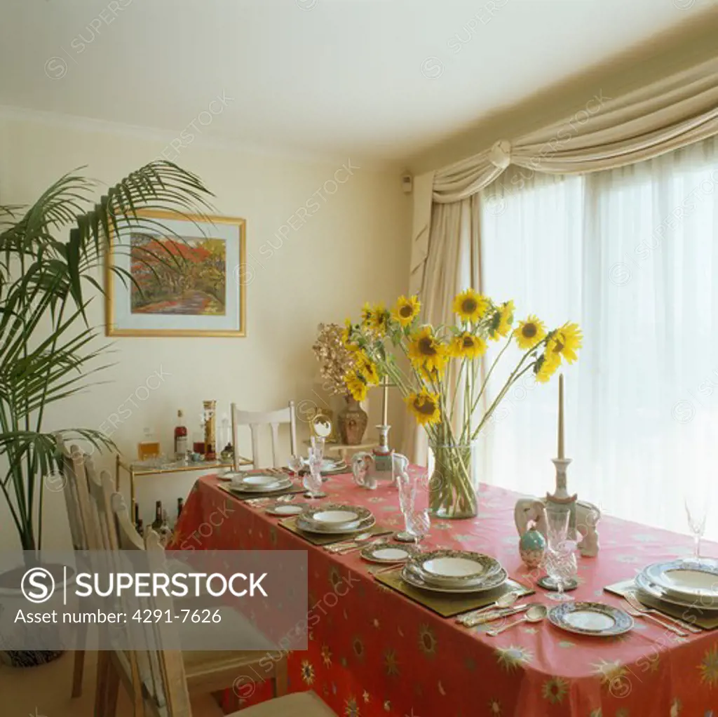 Vase of yellow sunflowers on table with red cloth in cream dining room