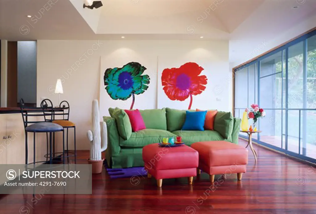 Pink stools and green sofa in front of flower paintings in modern living room with wooden flooring