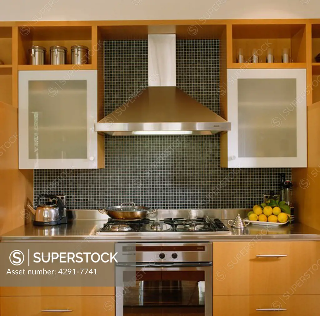 Stainless steel extractor and grey wall tiles above oven in modern kitchen