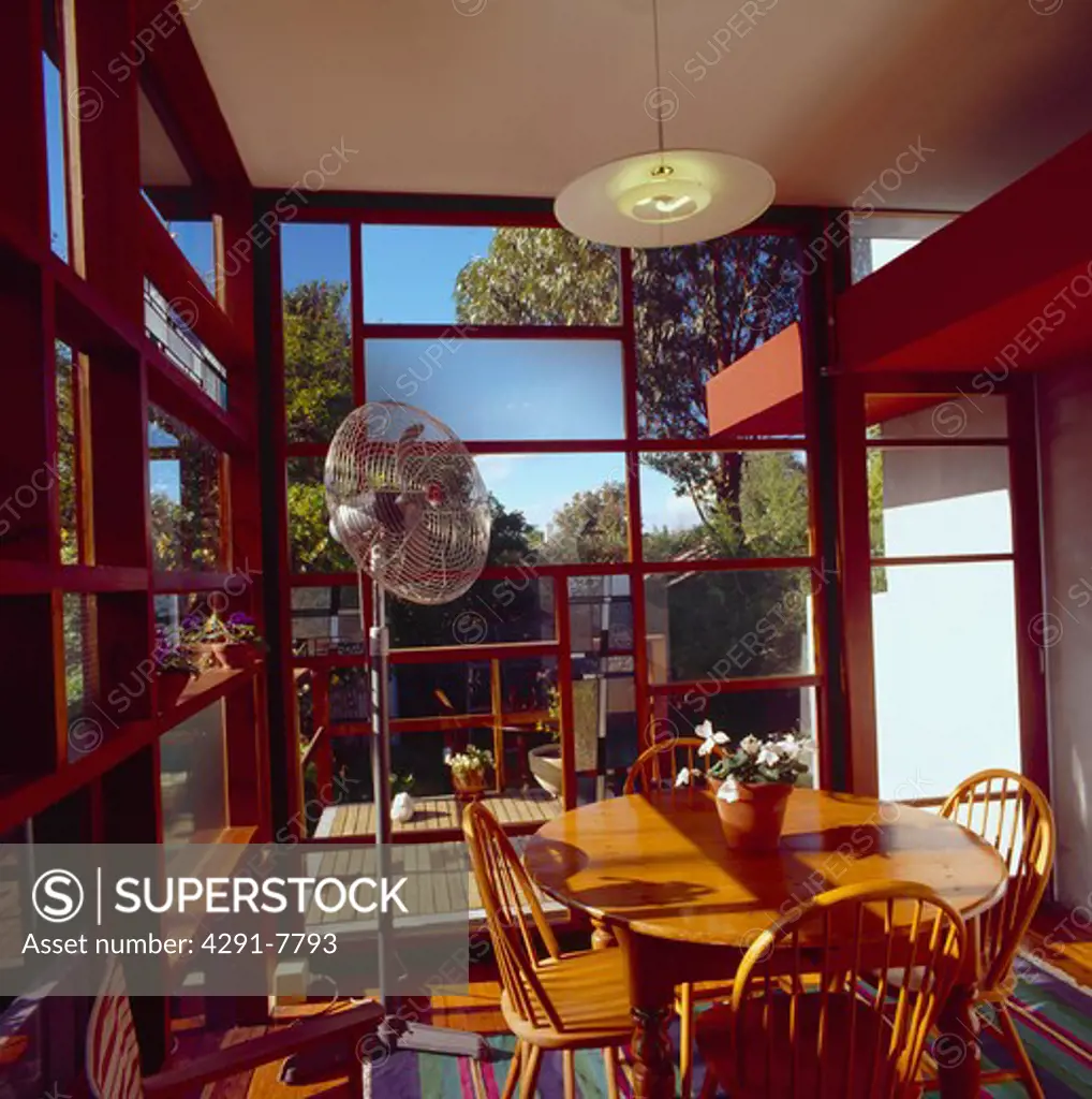 Ercol chairs and wooden table in modern dining room with large windows and view of decked patio