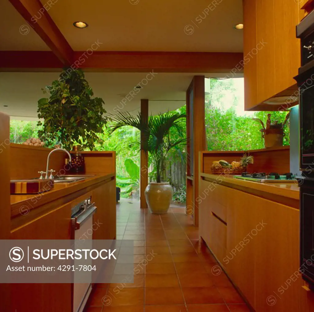 Modern kitchen with fitted wood units and large windows with view of tropical garden