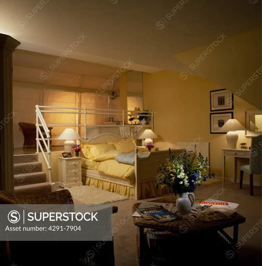 Lighted lamps in openplan yellow living and bedroom with yellow quilt and pillows on bed