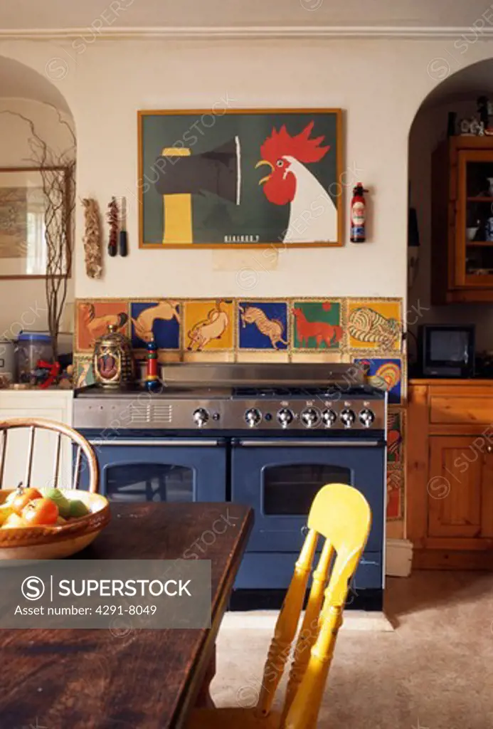Colourful tiles above blue range oven in country kitchen with old wooden table and chairs