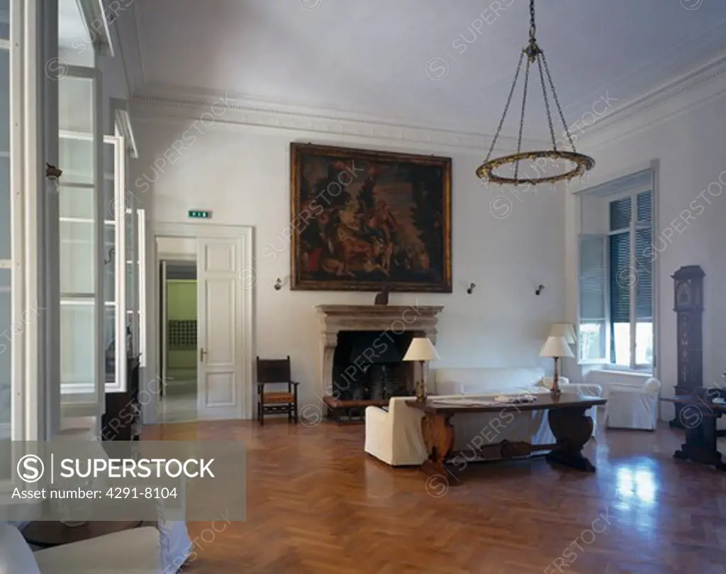 Large oil painting above fireplace in uncluttered drawing room with polished parquet flooring