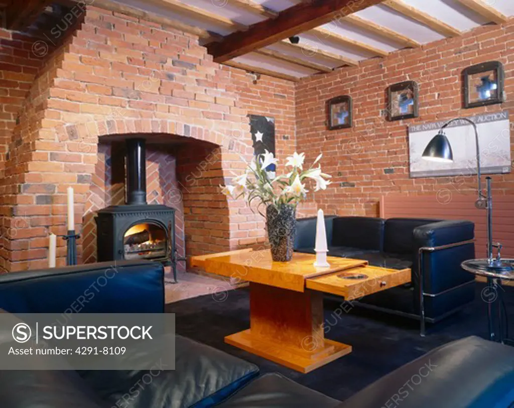 Brick walls and black leather sofas with modern wooden coffee table in living room with black stove in fireplace