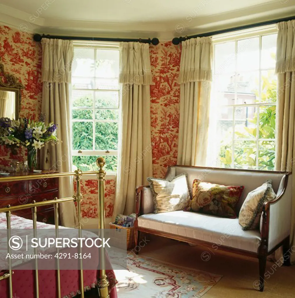 Red toile-de-Jouy wallpaper in bedroom with antique sofa in front of window