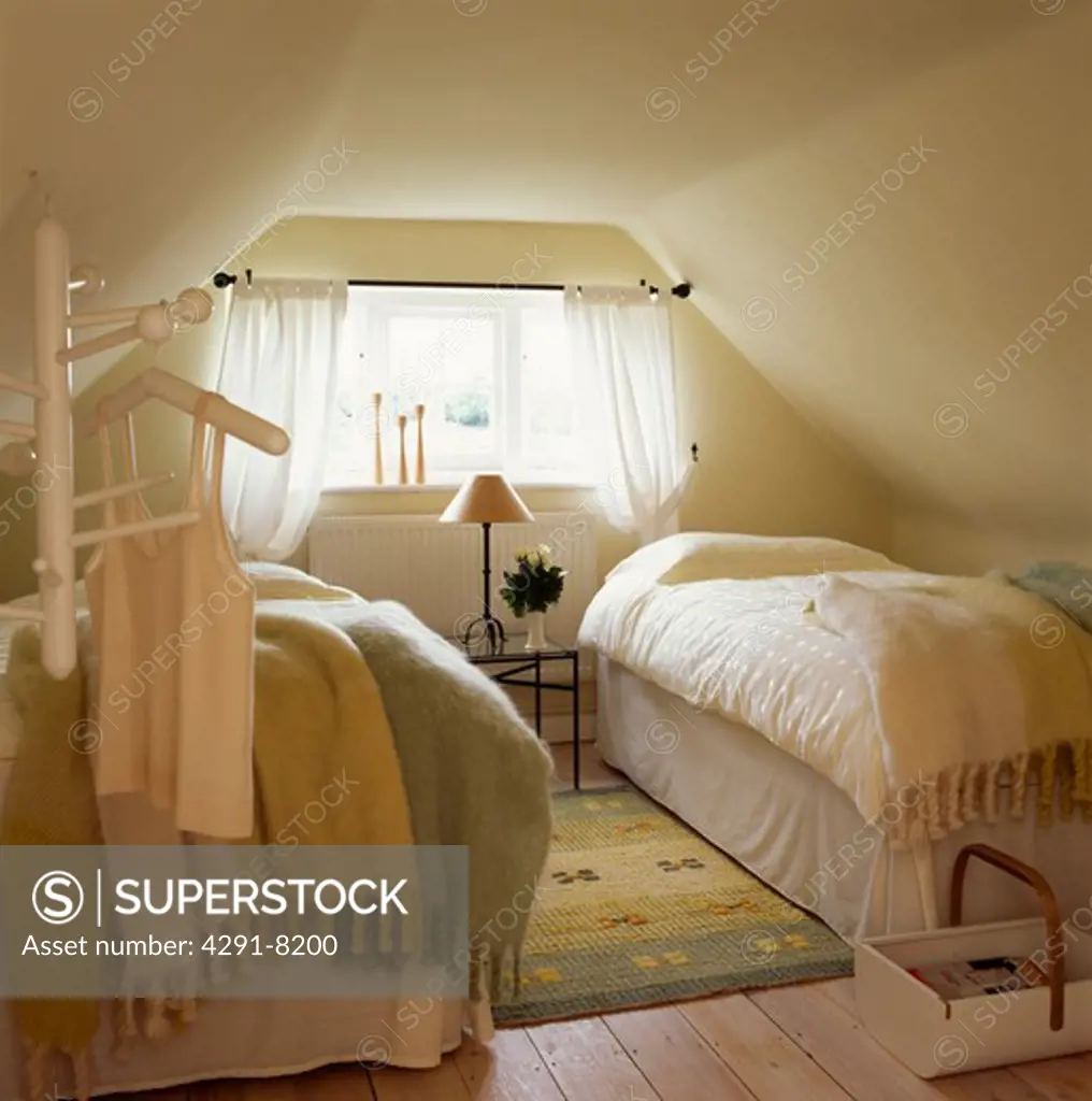 Mohair blankets and cream linen on twin beds in attic guest bedroom with patterned yellow rug on wooden flooring