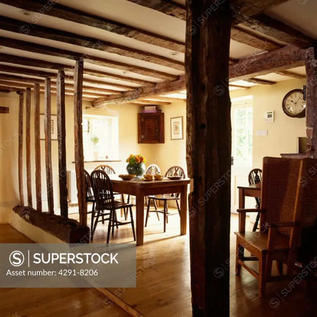 Wall beams with plaster removed in country dining room with wooden flooring and beamed ceiling
