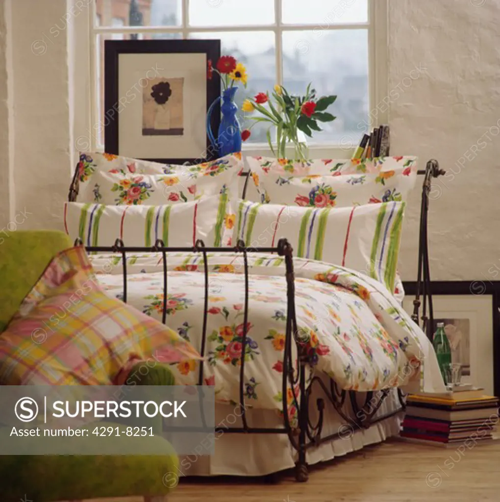 Striped and floral patterned pillows with floral quilt on wrought iron bed in front of window with picture on windowsill