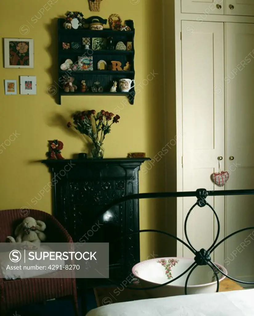 Miniature shelves above small black cast-iron fireplace in yellow bedroom with wrought-iron bed