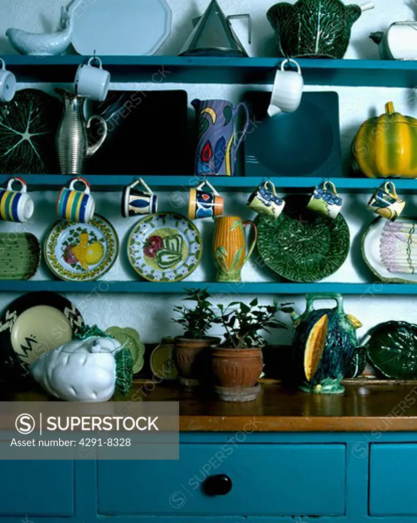 Pottery cups and plates on blue shelves above dresser with wooden top and blue base