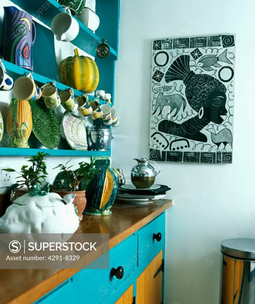 Colourful pottery on turquoise shelves above kitchen dresser and black and white picture on the wall