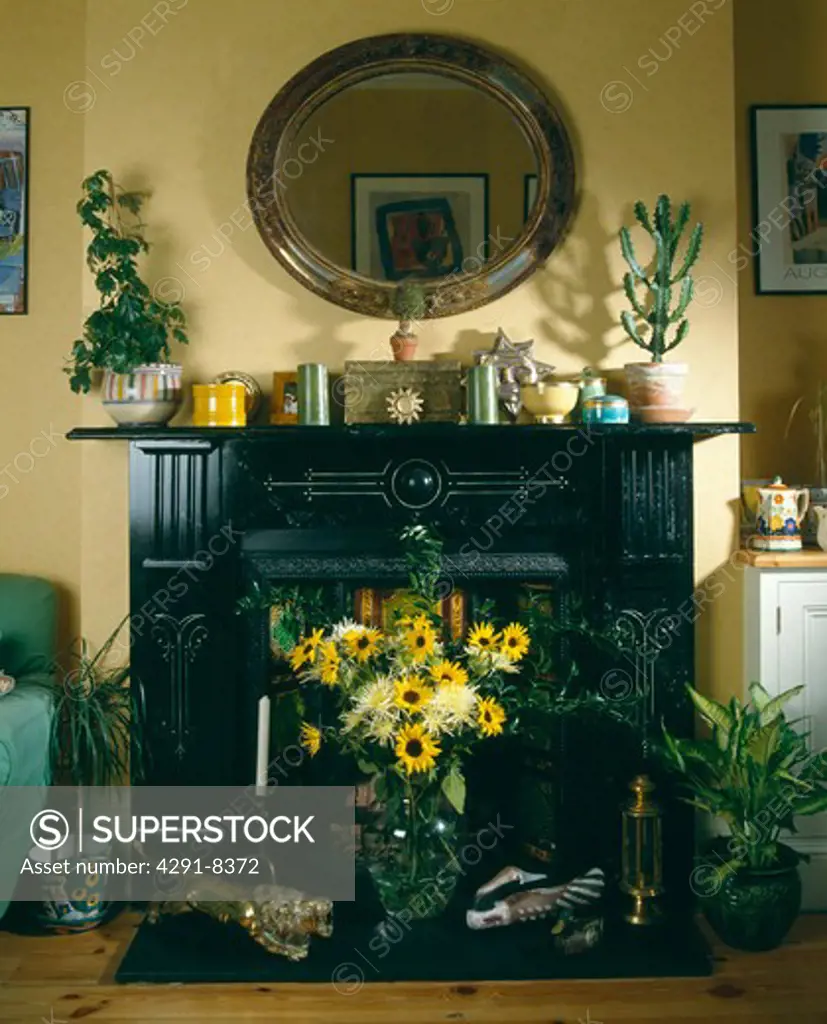 Mirror above black fireplace with yellow floral arrangement in grate in pastel yellow livingroom