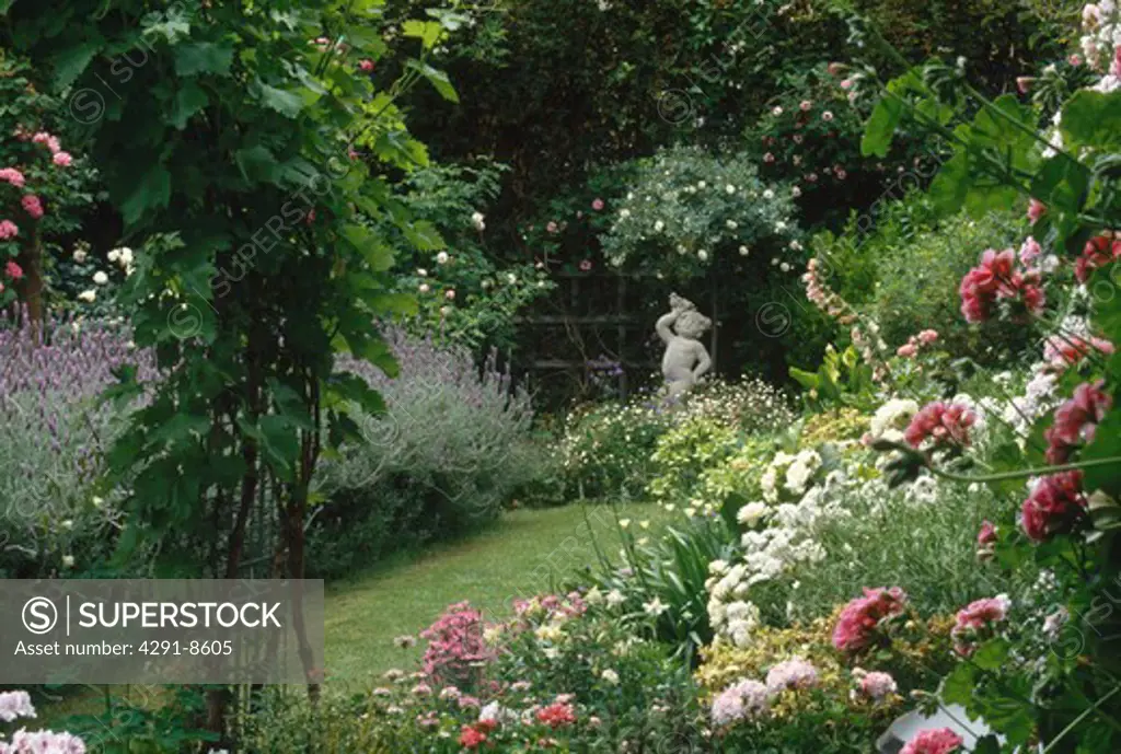 Pink and white roses and lavender on either side of grass path leading to statue of cherub below rose tree
