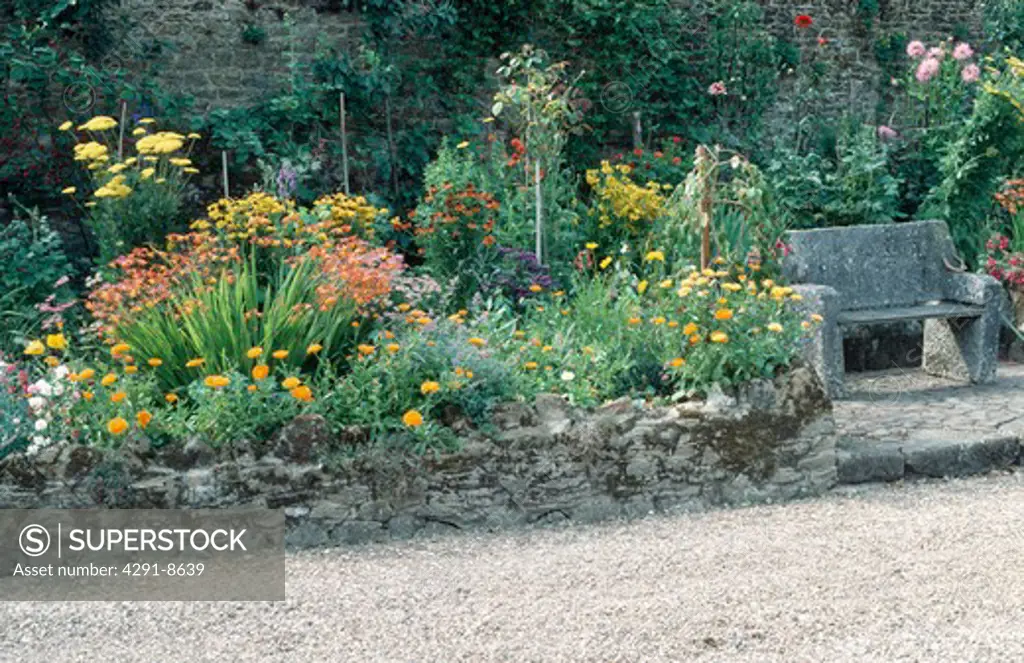 Orange calendula and hemerocallis with rudbeckia and astilbe in raised garden border beside stone seat