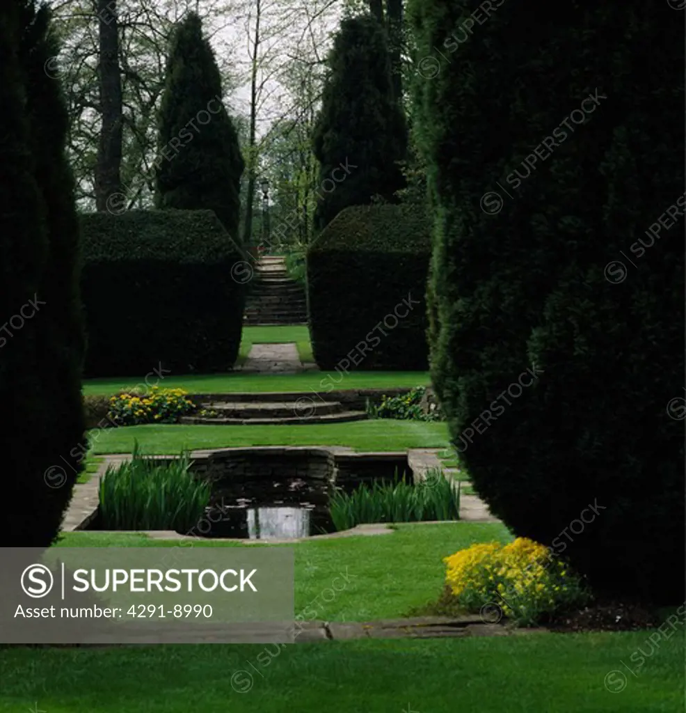 Calm vista over a small formal poolenclosed by clipped yew hedges and framed by tall Lawson cypresses