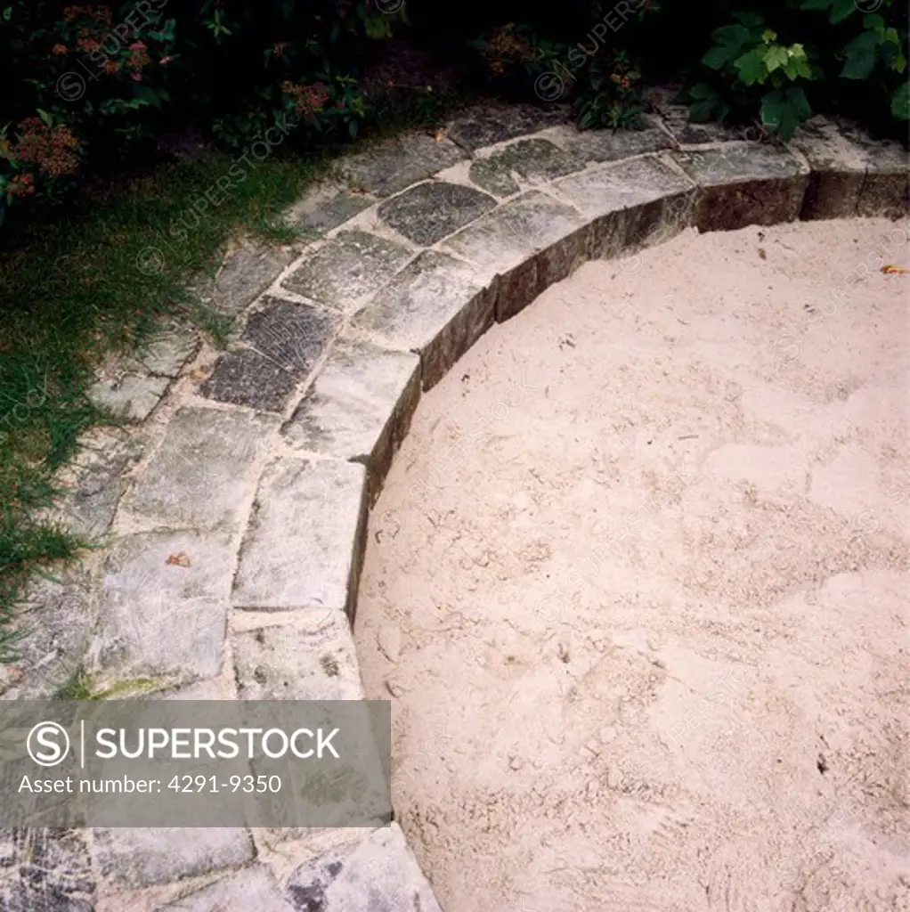 Circular sandpit with paved edging in children's play area in garden