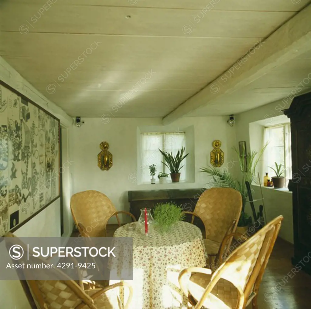 Cane chairs at small table with floral cloth in Scandinavian dining room with white painted wooden ceiling