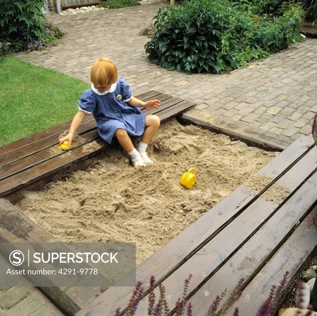 Small girl playing in sandpit in garden