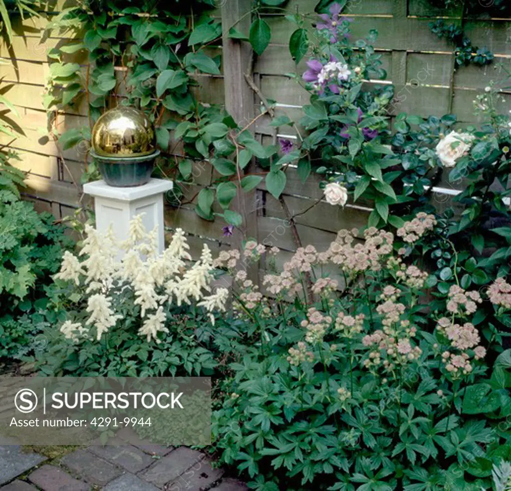 Brass globe on plinth in flower border in town garden in summer