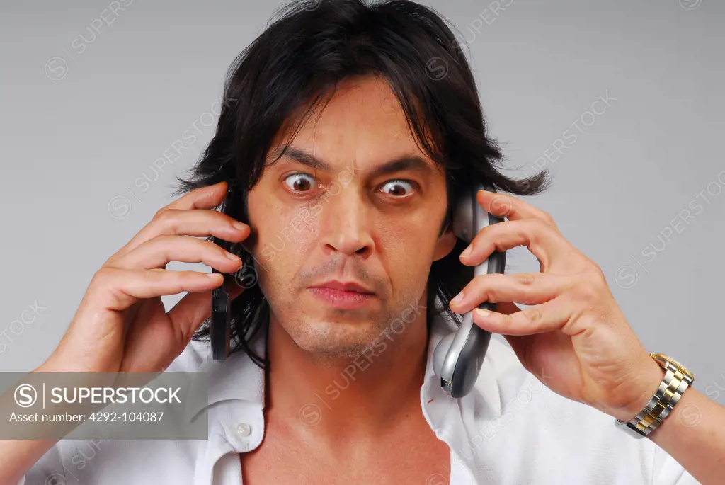 Close up of stressed man using two telephones