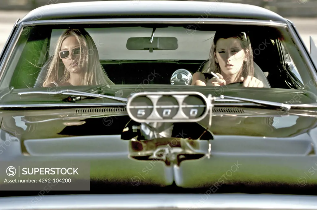 Two women sitting on vintage car