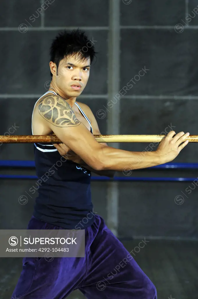 Portrait of a young man holding a wooden stick standing in a martial arts stance