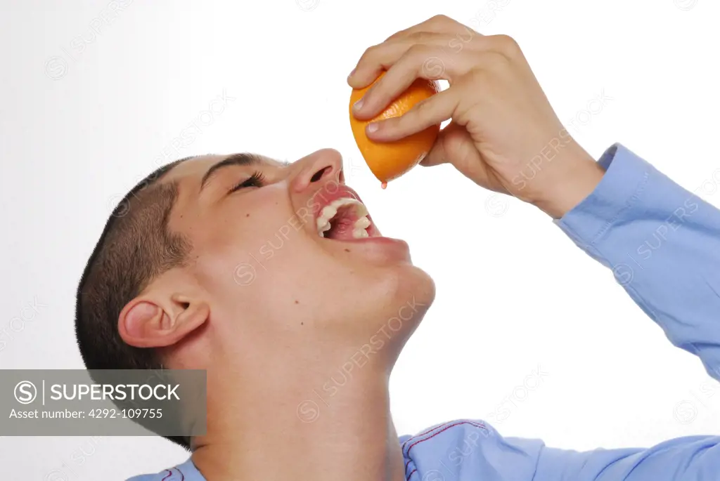 Teenage boy squeezing orange and drinking the juice