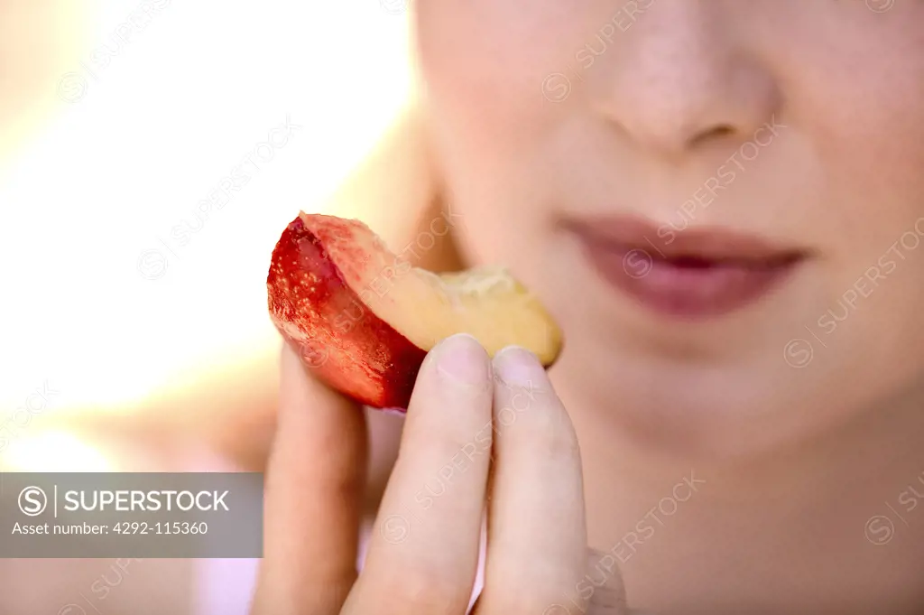Woman eating a slice of peach, close up
