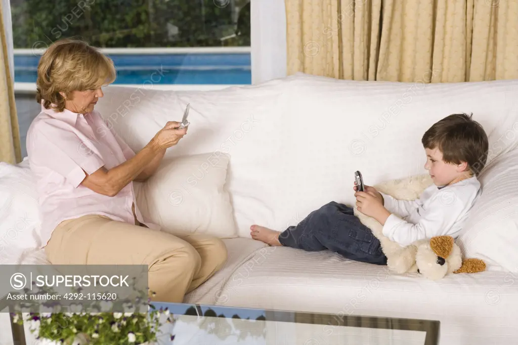 Grandmother and grandson sitting on sofa with mobiles