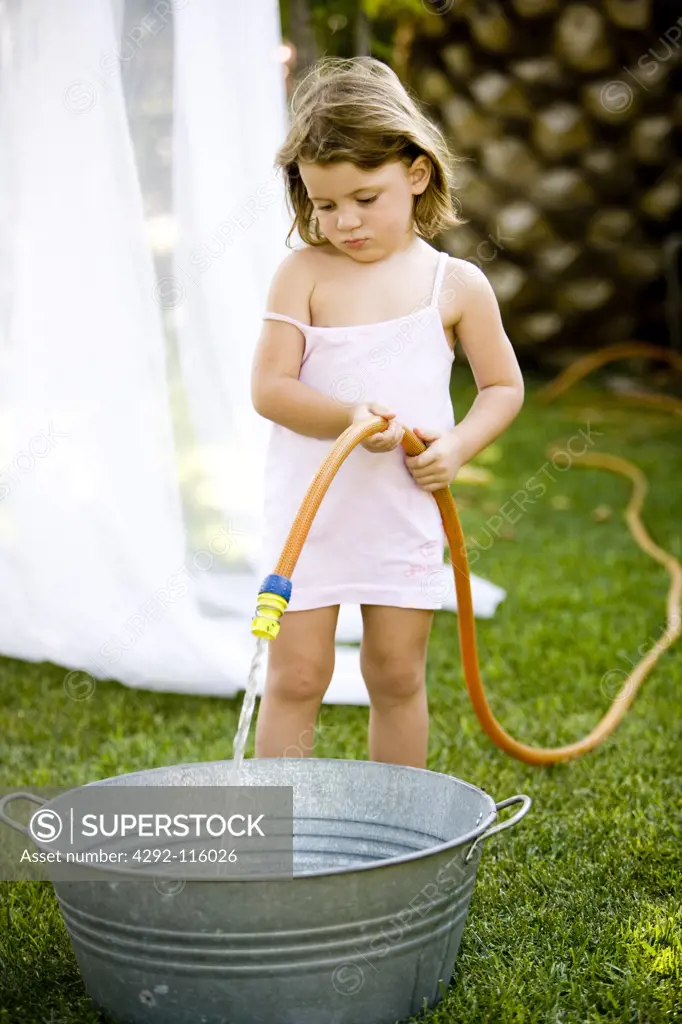 Little girl filling a basin with a hose