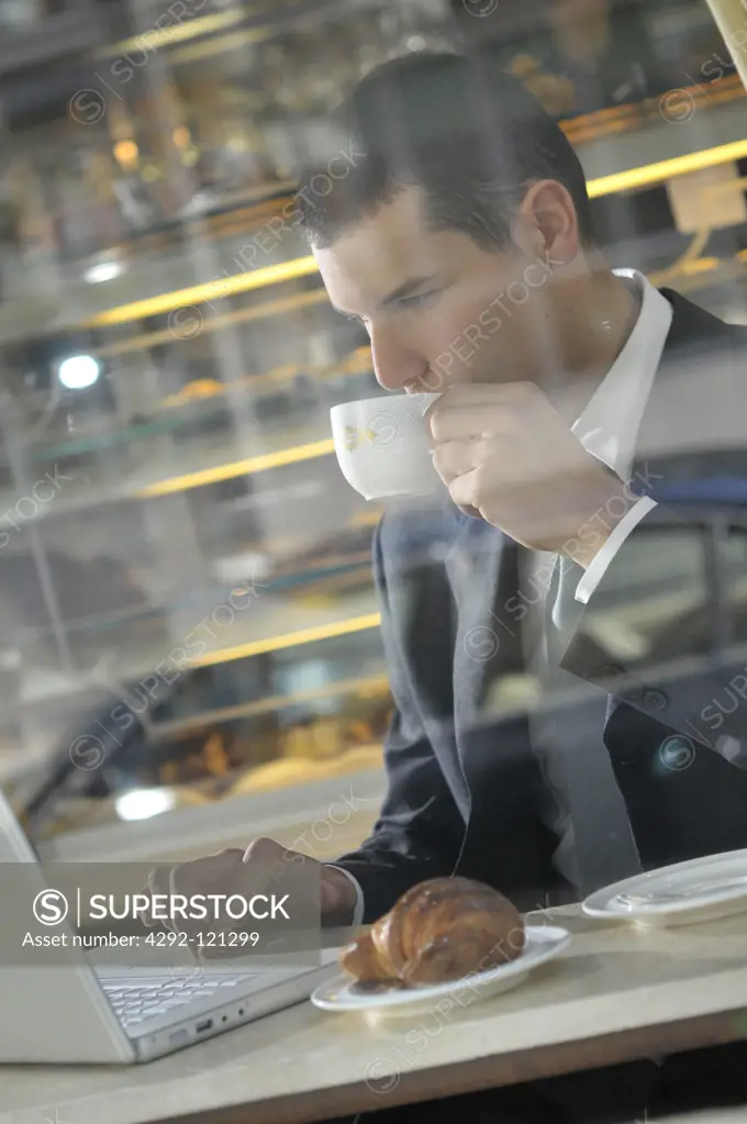 Businessman having breakfast in a cafe while using laptop